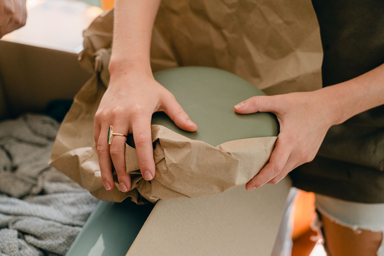 Glassware being wrapped in unprinted newsprint beside a dish pack carton